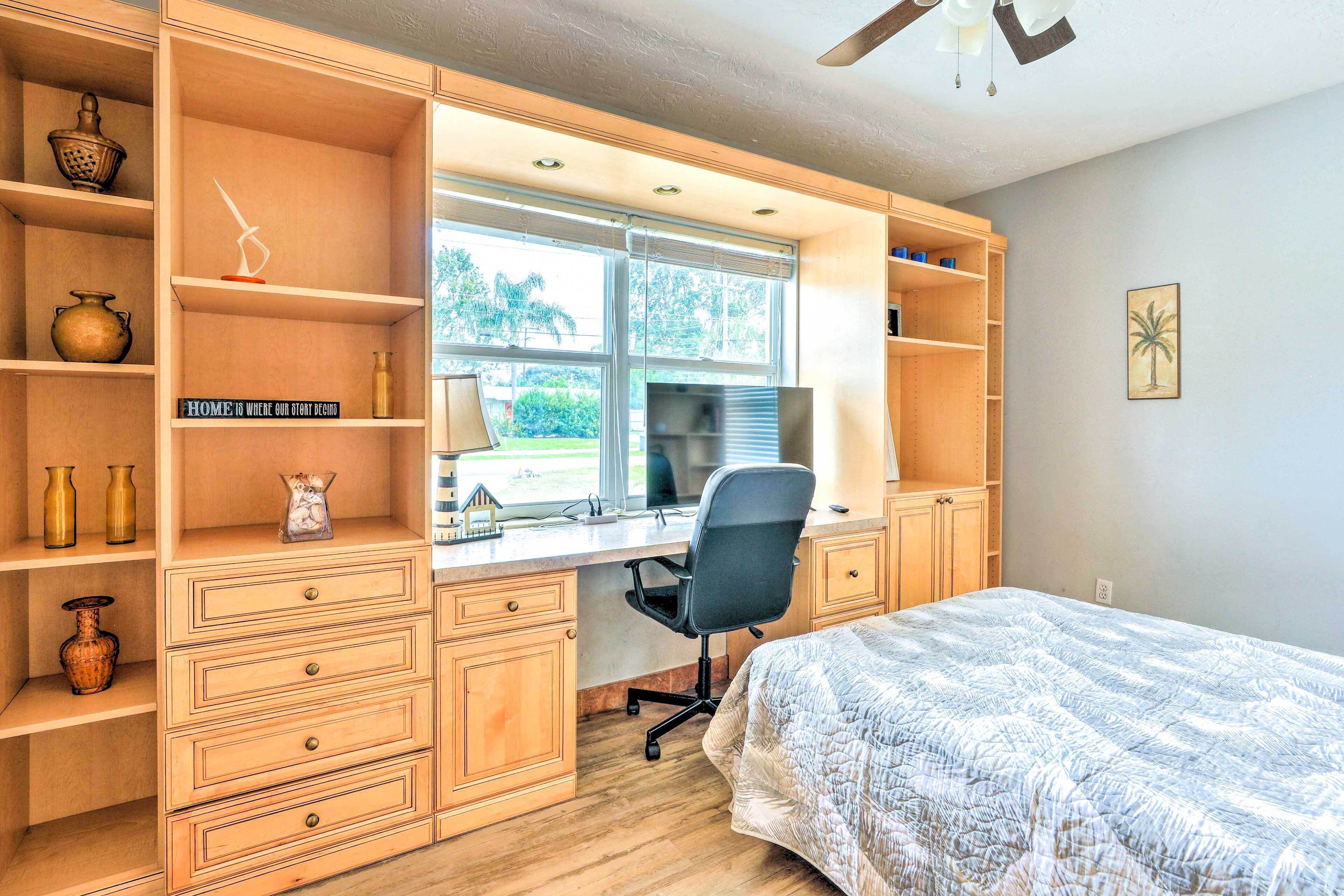 A bedroom with a bed, a desk with a computer, and shelves with decorative items.