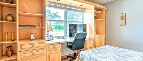 A bedroom with a bed, a desk with a computer, and shelves with decorative items.