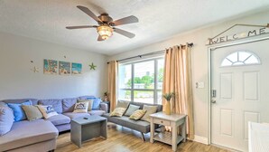 A living room with a sofa, coffee table, and a side table. There is a ceiling fan, a window with curtains, and a door with a 'WELCOME' sign. - 'ocean Breeze Oasis' w/ Boat Dock & Slip on Canal! (Bradenton)