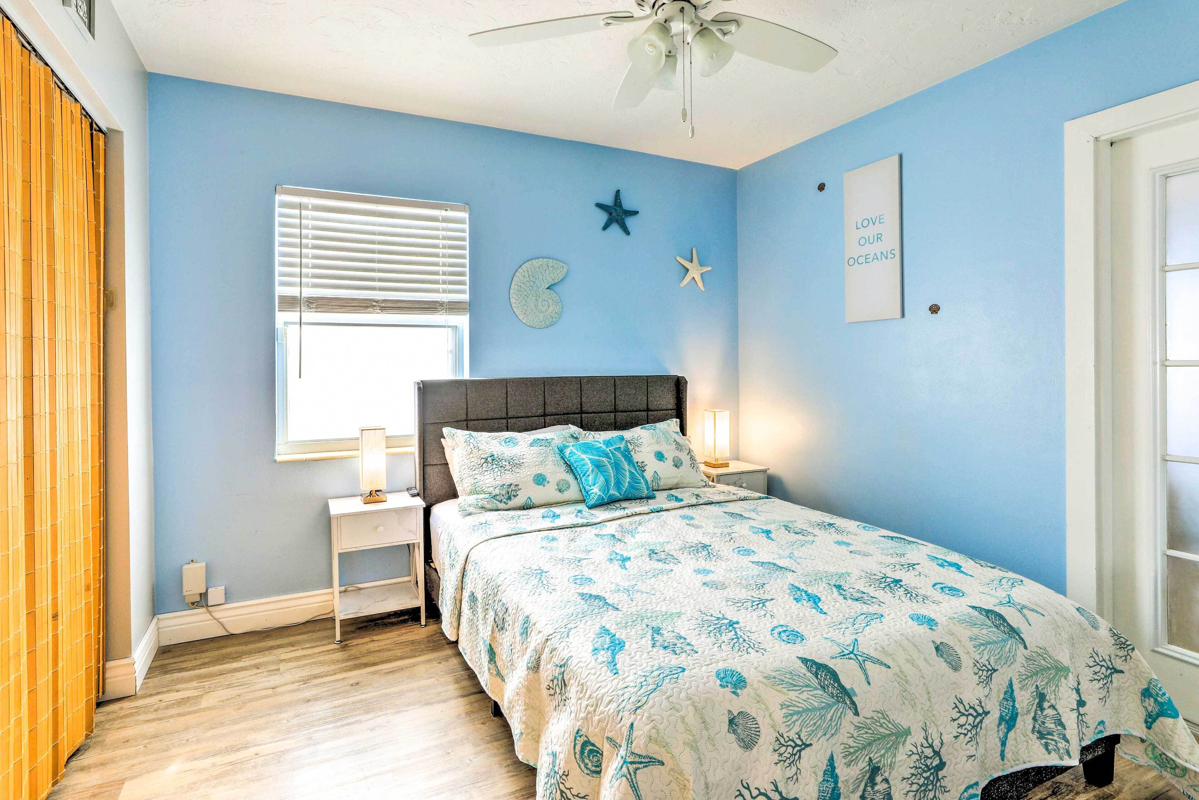 Une chambre à coucher comprenant un lit, des tables de chevet, un ventilateur de plafond, une fenêtre avec des stores et un mur décoré d’une étoile et d’une inscription.