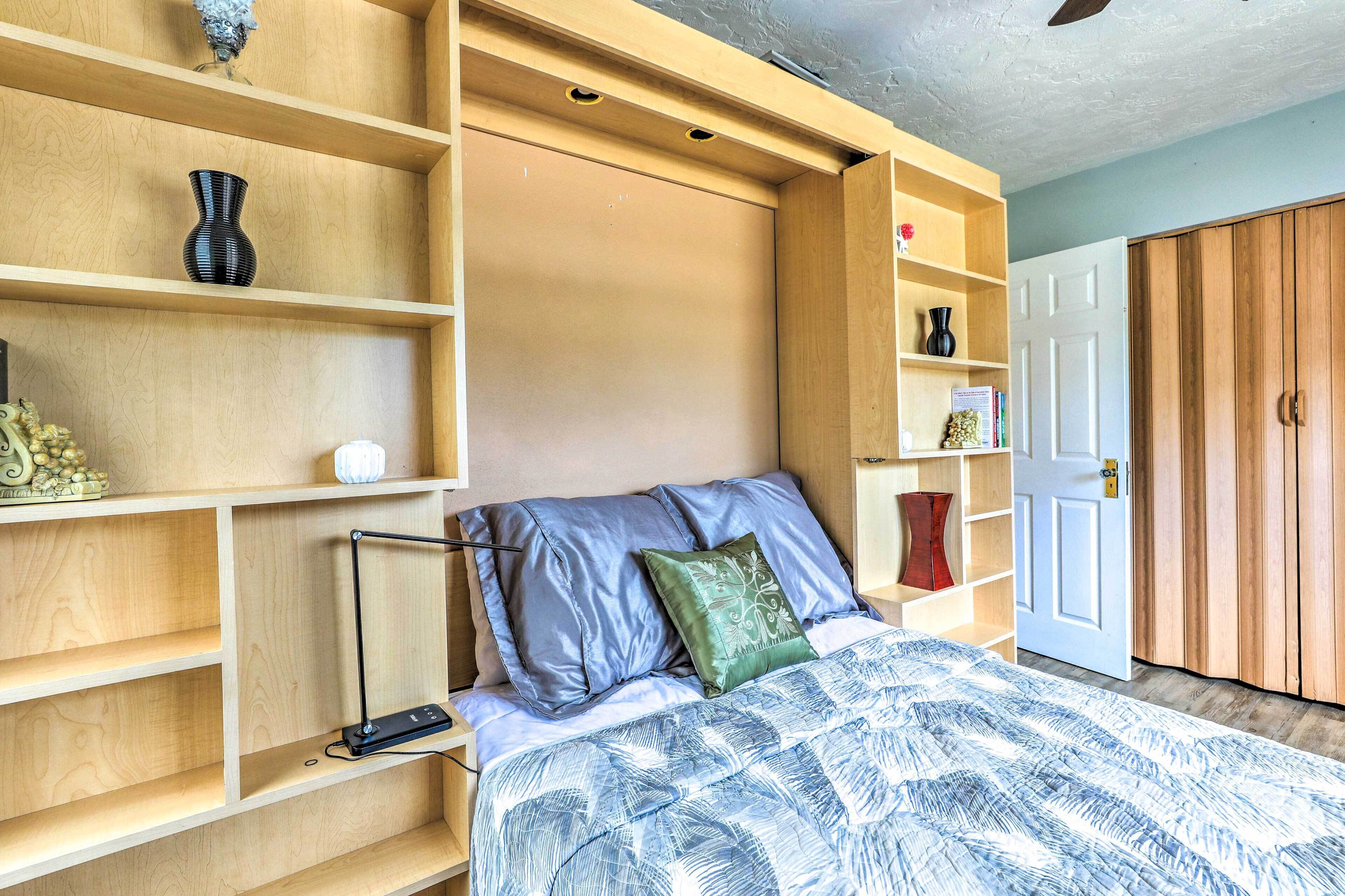 A bedroom with built-in shelves, a bed with a patterned bedspread, and a wardrobe.