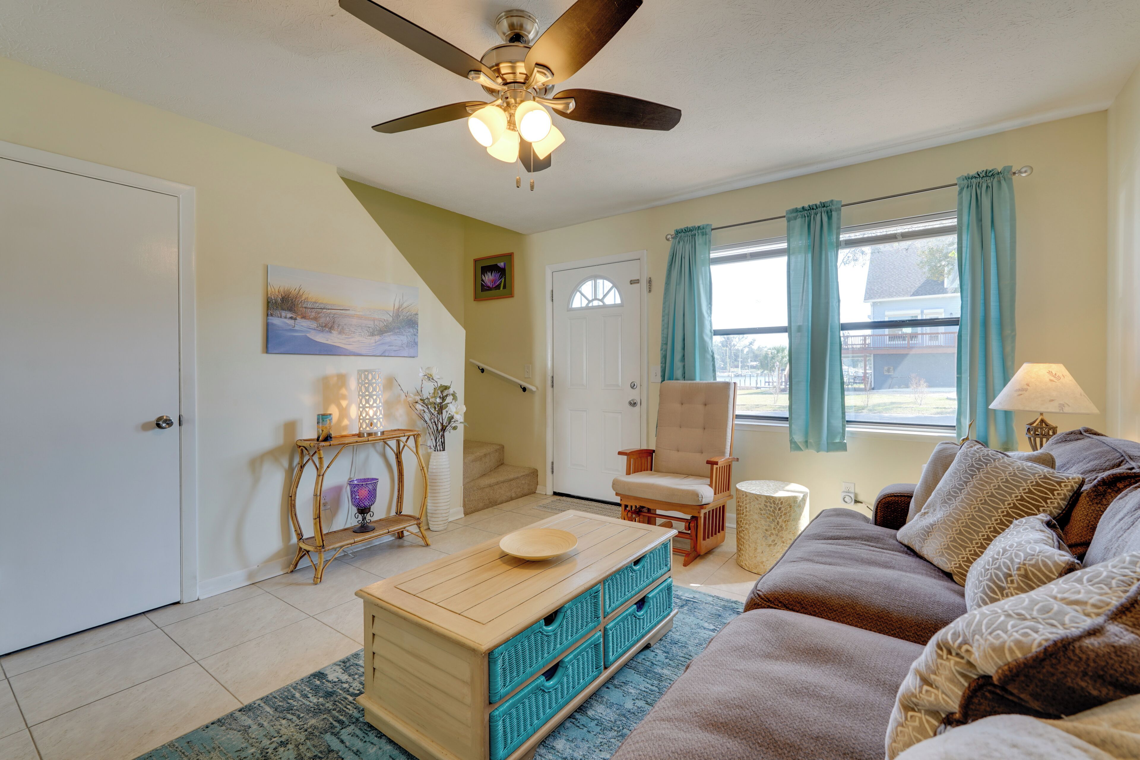 A well-lit living room with a ceiling fan, a sofa, a coffee table, and a window with curtains.
