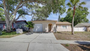 A residential driveway leading to a house with a garage, surrounded by trees and a lawn. - Pet-friendly Home w/ Pool in Palm Harbor! (Palm Harbor)