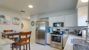A modern kitchen with stainless steel appliances, a granite countertop, and a dining area with wooden chairs and a table. - Pet-friendly Home w/ Pool in Palm Harbor! (Palm Harbor)