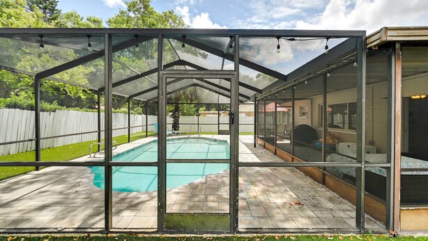 A glass-enclosed pool area with a clear view of the pool, surrounded by a wooden deck and a white fence. - Pet-friendly Home w/ Pool in Palm Harbor! (Palm Harbor)