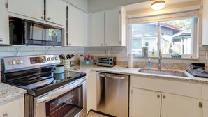 A kitchen with white cabinets, stainless steel appliances, a window with blinds, and a countertop with various items. - Pet-friendly Home w/ Pool in Palm Harbor! (Palm Harbor)