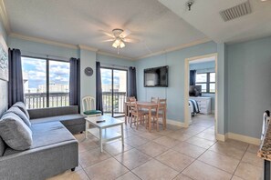 Un salon comprenant un canapé, une table à manger avec des chaises, un ventilateur de plafond et un téléviseur fixé au mur.