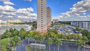 A high-rise hotel with a central tower, surrounded by a parking lot and palm trees.