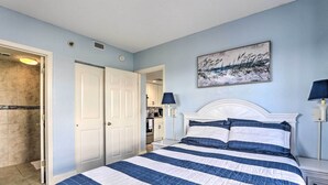A bedroom with a bed, two bedside tables, a nightstand, a painting, and a door leading to a bathroom.