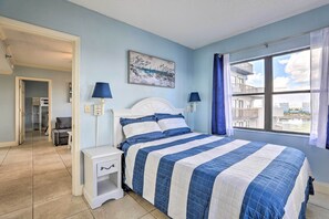 Une chambre à coucher avec un lit, des tables de chevet, un tableau et une vue sur un immeuble par la fen être.