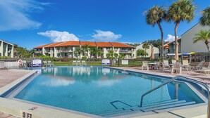 A swimming pool with a clear blue water surface, surrounded by lounge chairs and a building with a red-tiled roof. - Ocean Views + Pool Access: Tierra Verde Condo! (Tierra Verde)