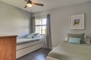 Une chambre avec deux lits, un ventilateur de plafond, une fenêtre avec des rideaux et un tableau encadré au mur.