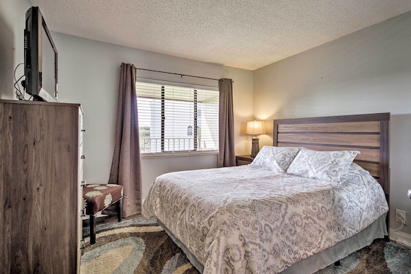 A bedroom with a bed, a wooden wardrobe, a nightstand with a lamp, and a window with curtains.