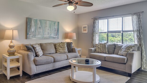 A living room with two sofas, a coffee table, a ceiling fan, and a window with curtains. - Ocean Views + Pool Access: Tierra Verde Condo! (Tierra Verde)