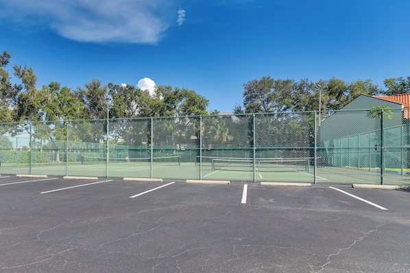 Un court de tennis clôturé, avec plusieurs places de stationnement et un bâtiment écologique en arrière-plan.
