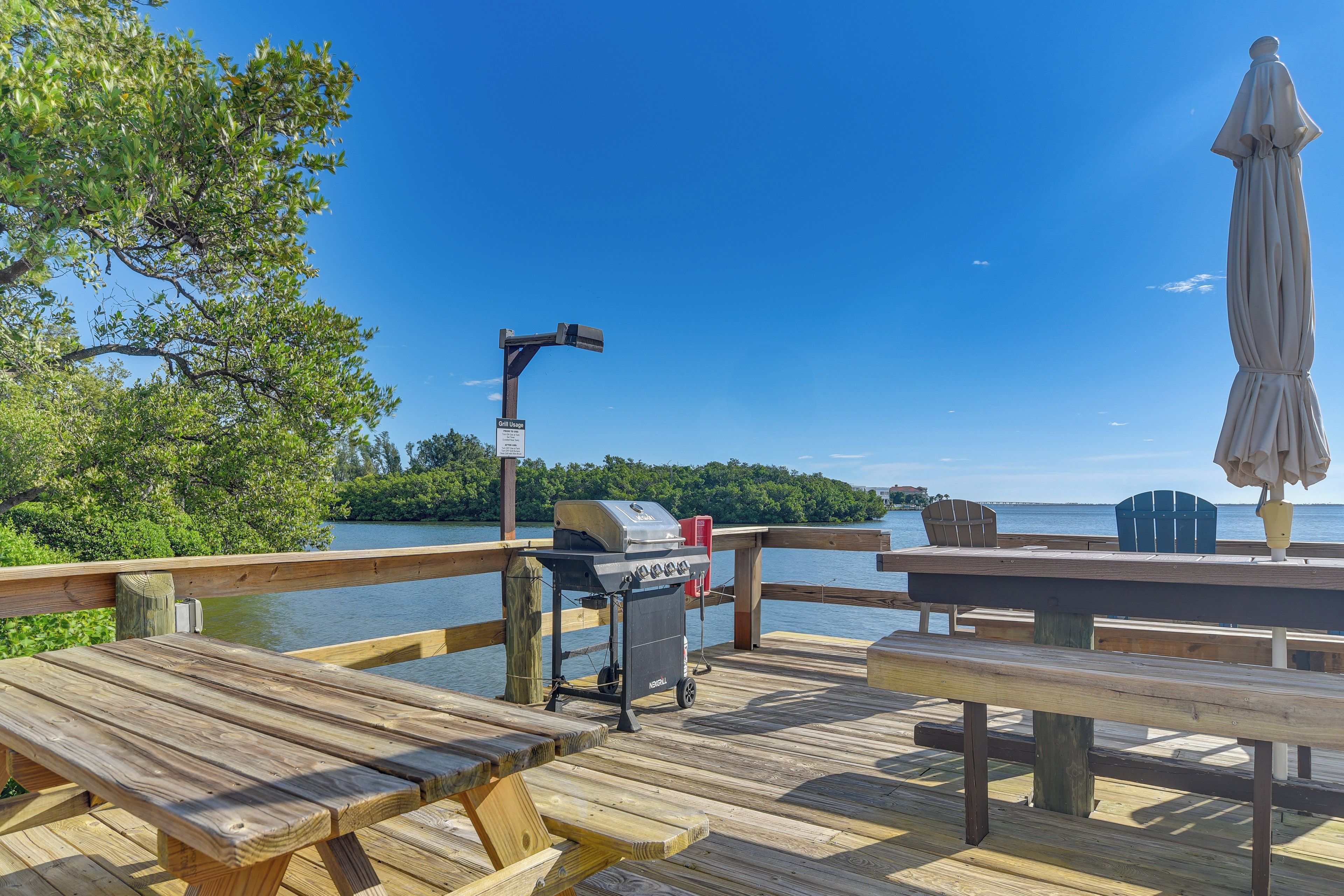A wooden deck with picnic tables and a grill, overlooking a body of water.