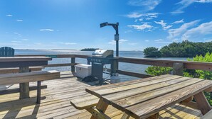 A wooden deck with picnic tables and a grill, overlooking a body of water with a clear sky. - Ocean Views + Pool Access: Tierra Verde Condo! (Tierra Verde)