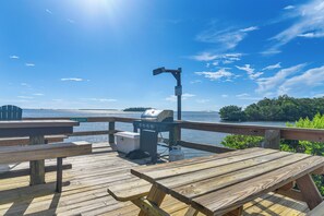 Un molo in legno con tavoli da picnic e un barbecue, affacciato su uno specchio d'acqua sotto un cielo sereno.