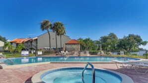 A swimming pool area with a hot tub, lounge chairs, and a fenced pool area with palm trees. - Ocean Views + Pool Access: Tierra Verde Condo! (Tierra Verde)