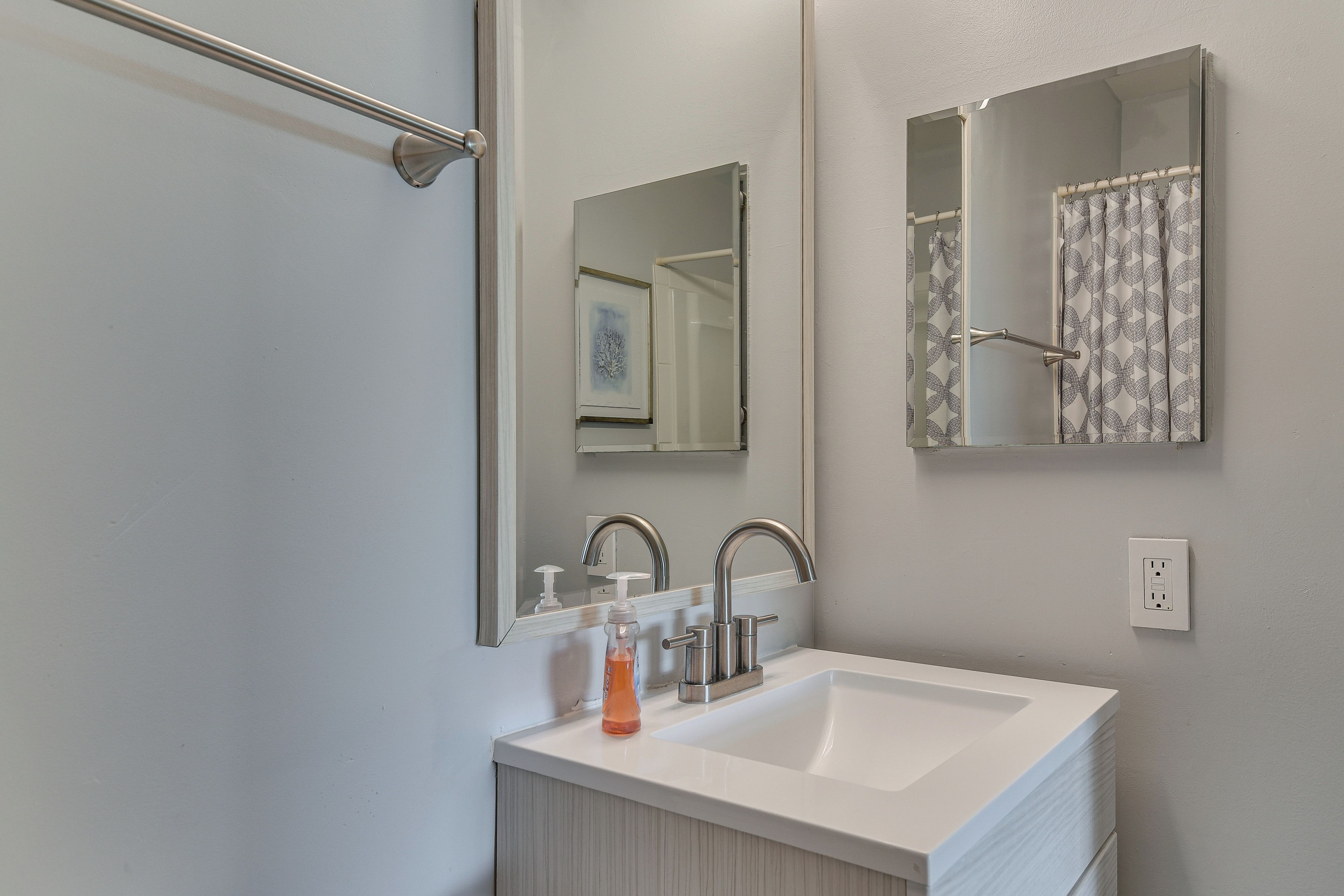 A bathroom with a white sink, two faucets, a mirror, and a shower curtain.