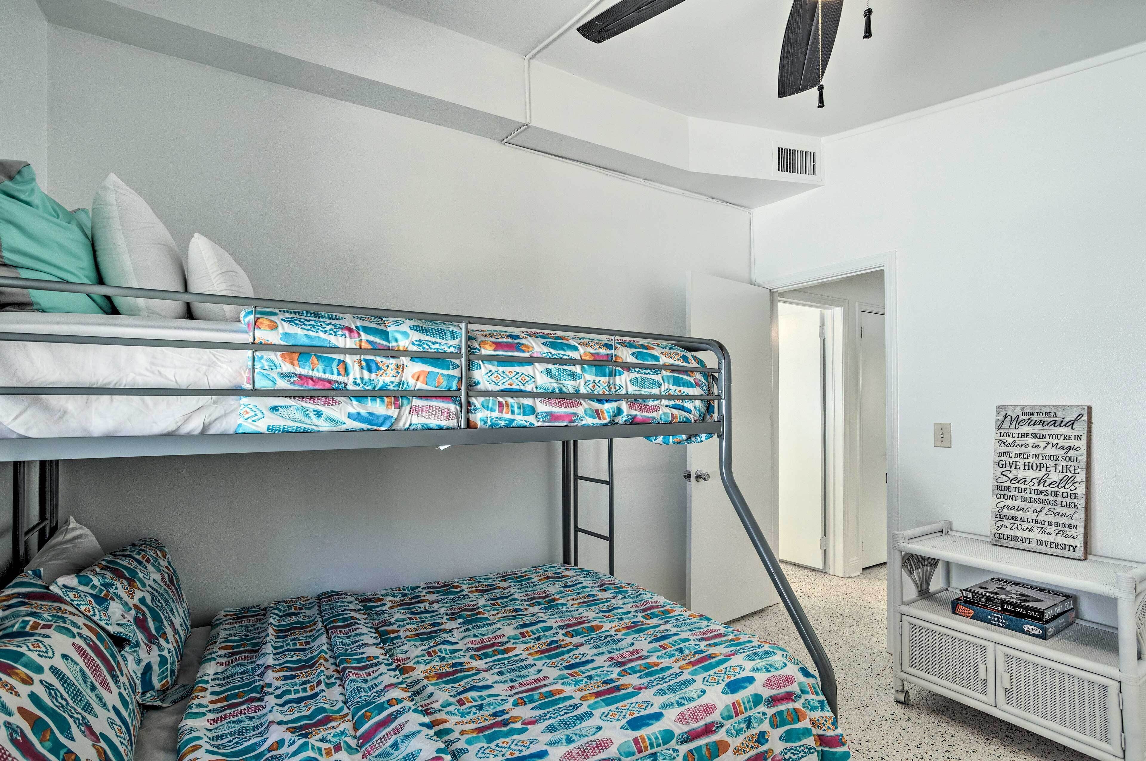 Un letto a castello con biancheria decorata, una parete bianca e un piccolo ripiano con libri.