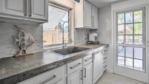 A kitchen with white cabinets, a large window, and a sign that reads "Beach House." - Palm City Canalfront Home w/ Boat Dock & Fire Pit! (Palm City)