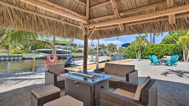 A covered outdoor seating area with wicker furniture, a grill, and a view of a marina with boats. - Palm City Canalfront Home w/ Boat Dock & Fire Pit! (Palm City)