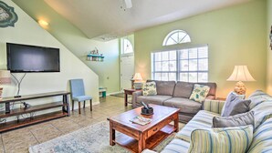 A living room with a flat-screen TV, wooden coffee table, striped sofa, and a ceiling fan.