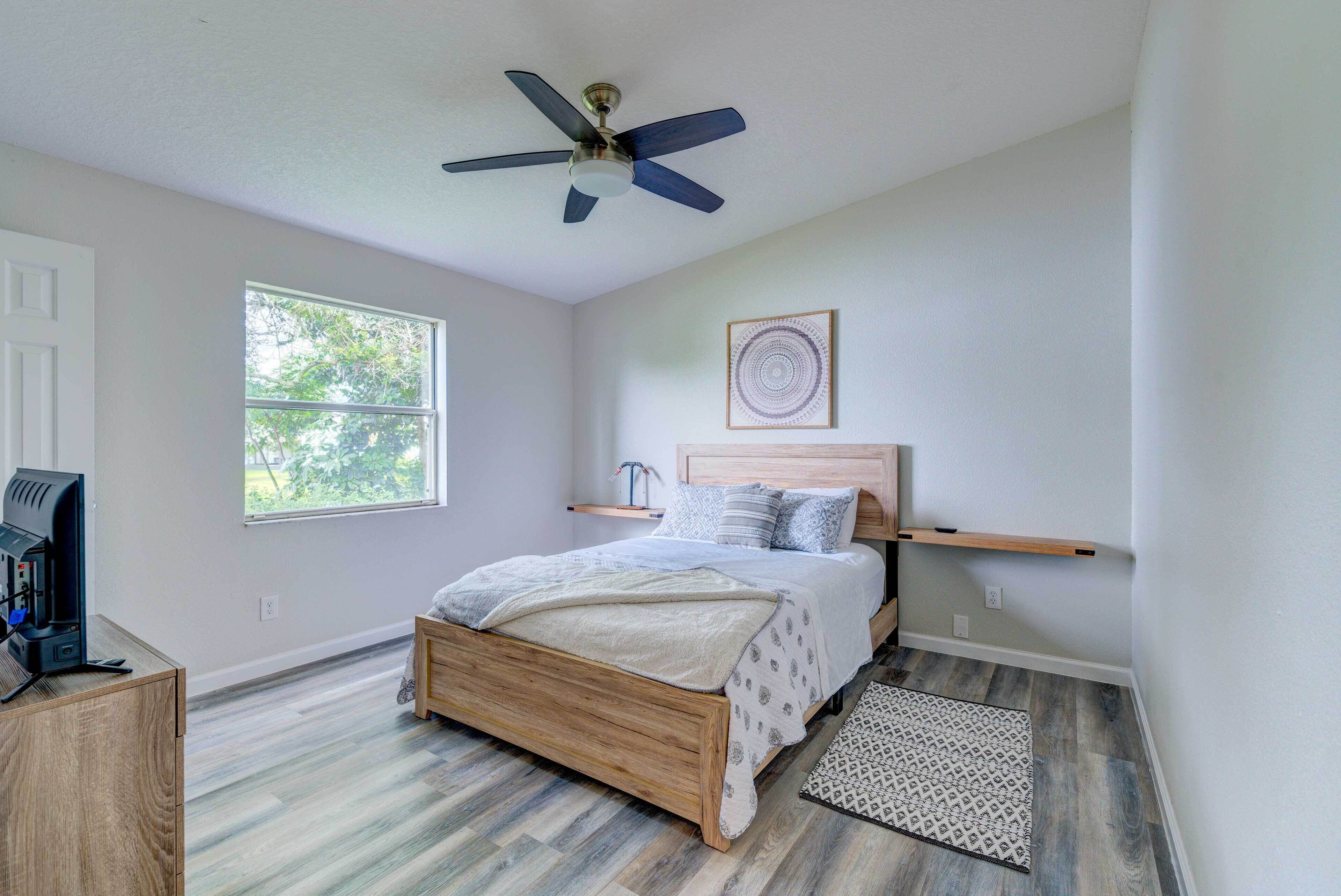 A bedroom with a wooden bed, a ceiling fan, a window, and a small desk with a coffee maker.