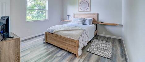 A bedroom with a wooden bed, a ceiling fan, a window, and a small desk with a coffee maker.