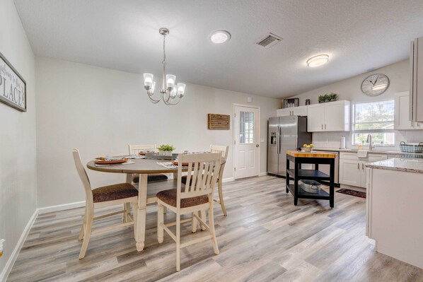Une cuisine moderne avec des meubles blancs, une table à manger en bois et un lustre.