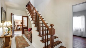 Una escalera con balaustres de madera, un tapete, una lámpara y un sofá en una habitación con paredes blancas y suelo de madera.