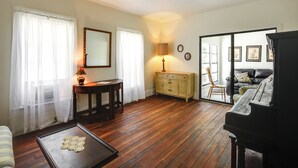 Una sala de estar con piso de madera, un piano, un sofá, una mesa de centro, una lámpara, una mesita auxiliar y un armario.