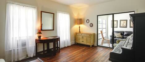 Un salon doté d’un parquet en bois, d’un piano, d’un canapé, d’une table basse, d’une lampe, d’une table d’appoint et d’un meuble.