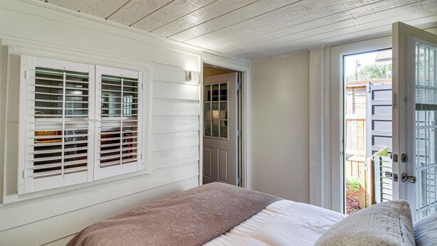 Ein Schlafzimmer mit Bett, einem Fenster mit Jalousien und einer Tür, die auf einen Balkon führt.