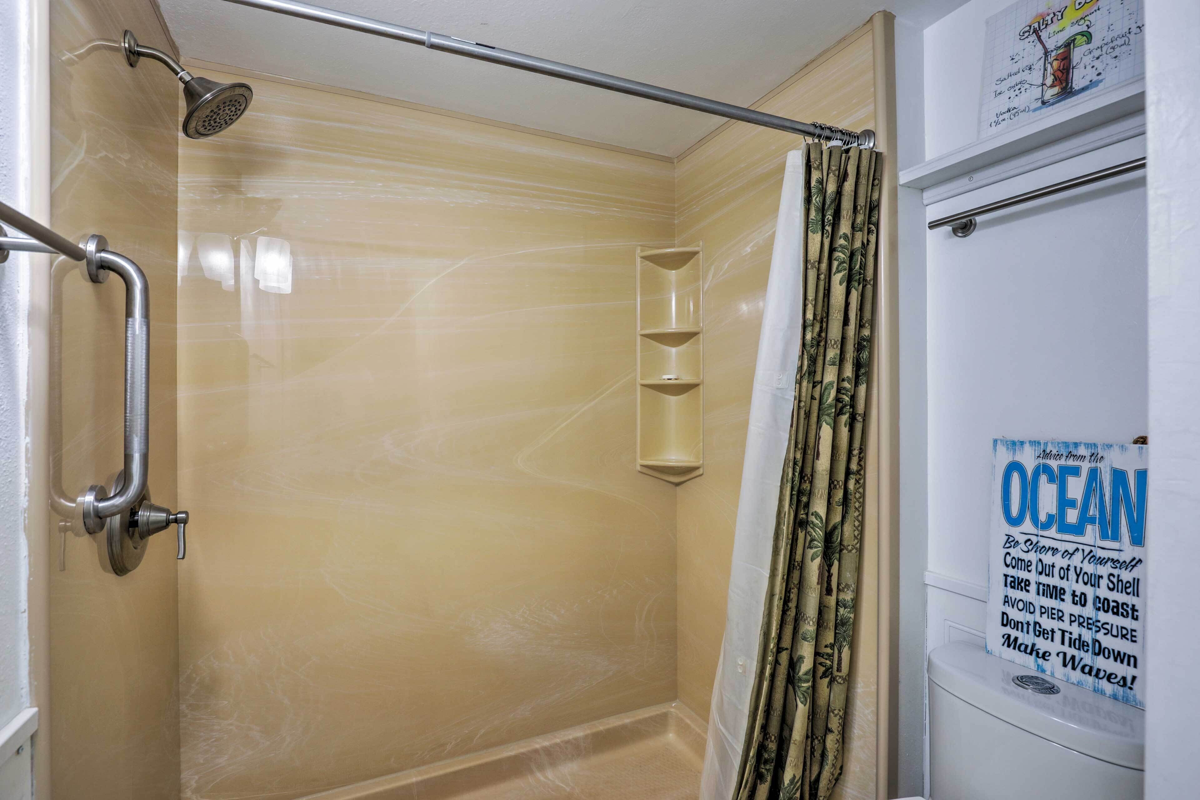 A bathroom with a shower, a handrail, a towel rack, and a poster on the wall.