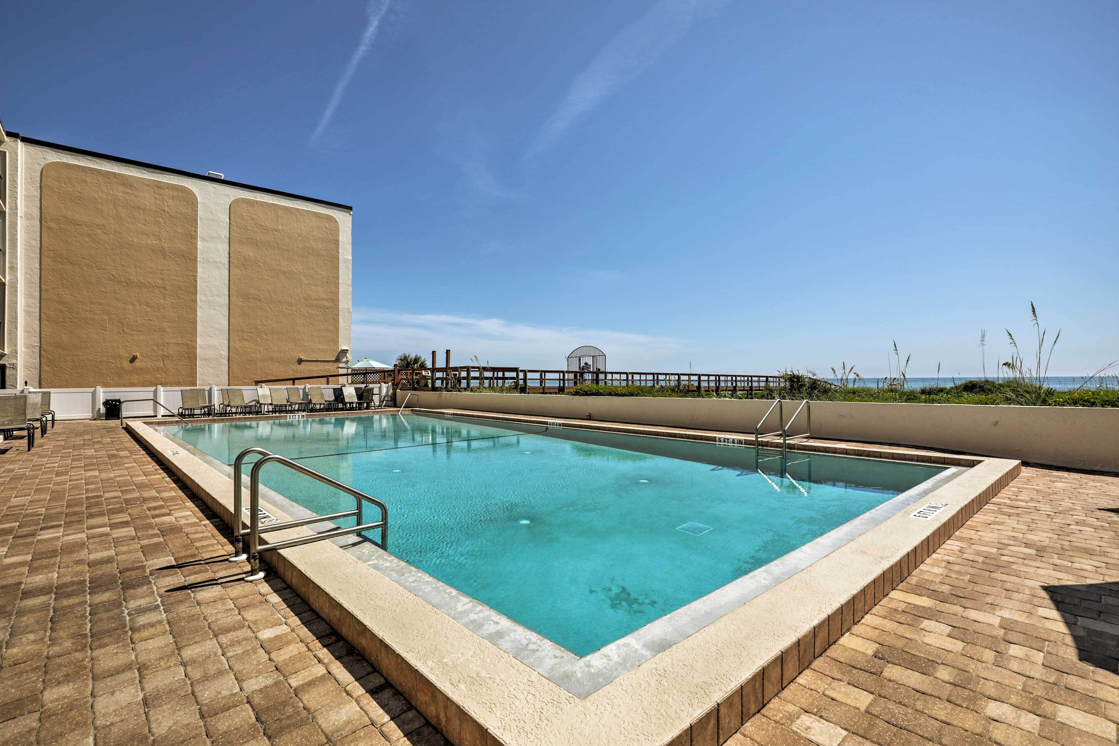 A rectangular pool with a tiled deck, a metal ladder, and a view of the ocean.