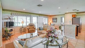 A spacious living room with a television, comfortable seating, a glass coffee table, and a kitchen area with a refrigerator and cabinets. - Cozy Frostproof Escape w/ Private Hot Tub! (Frostproof)