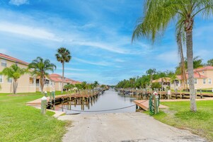 A canal with wooden docks and boats, surrounded by palm trees and buildings with red roofs.