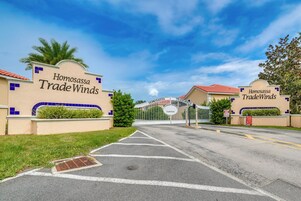 Una entrada con portón a Homosassa Trade Winds, con cielo despejado y palmeras.