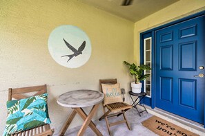 A blue door, a round table, a folding chair, a bench, a wall with a bird mural, and a potted plant. - Private Pool & Grill: Peaceful Home in Dunnellon (Dunnellon)