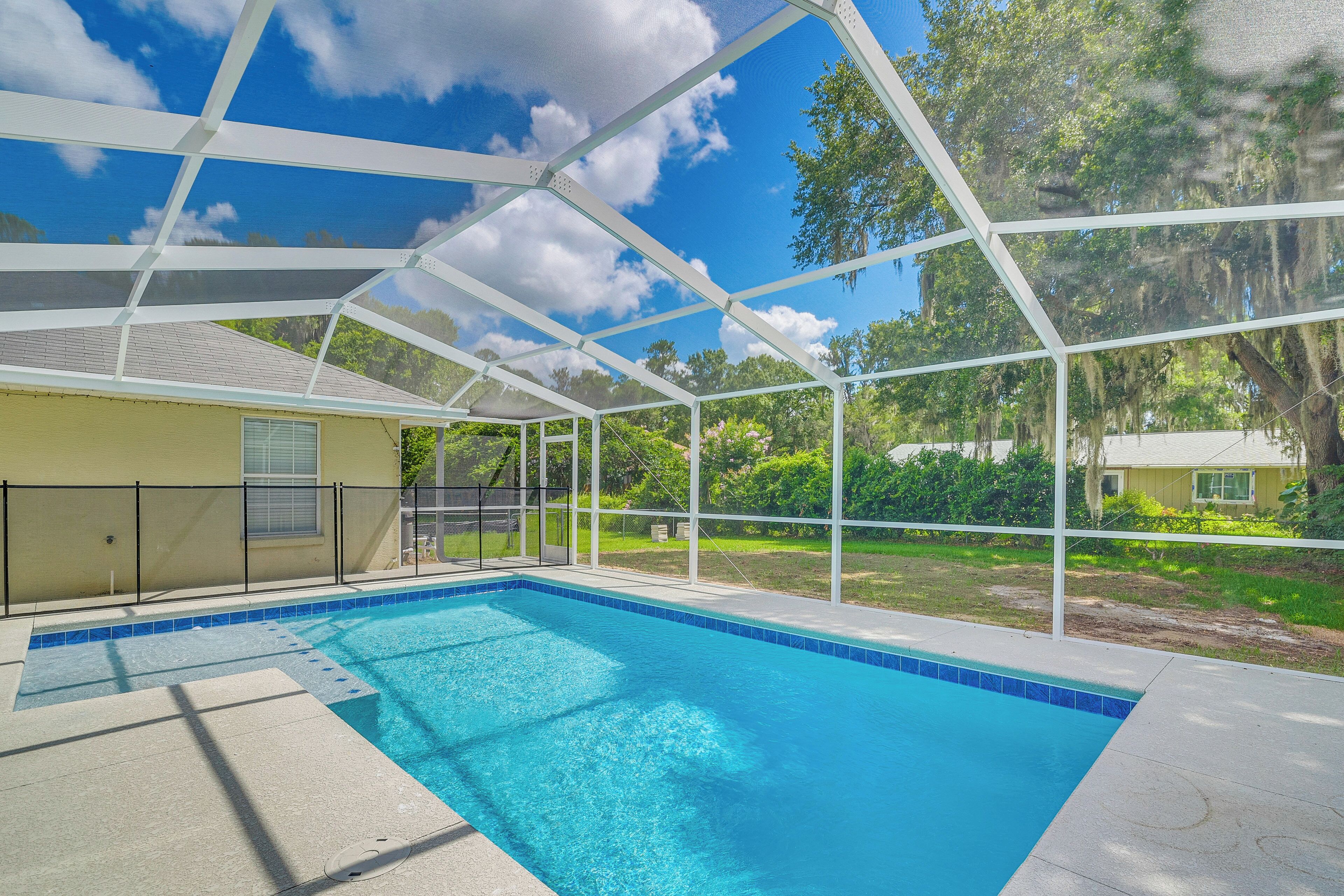 A covered swimming pool with a clear blue water, surrounded by a white metal frame and a black fence.