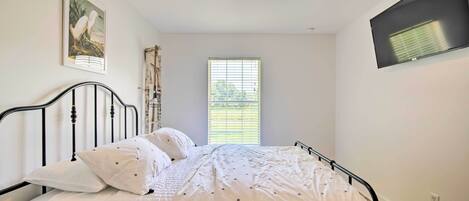 A bedroom with a bed, a ceiling fan, a window with blinds, and a wall-mounted TV.