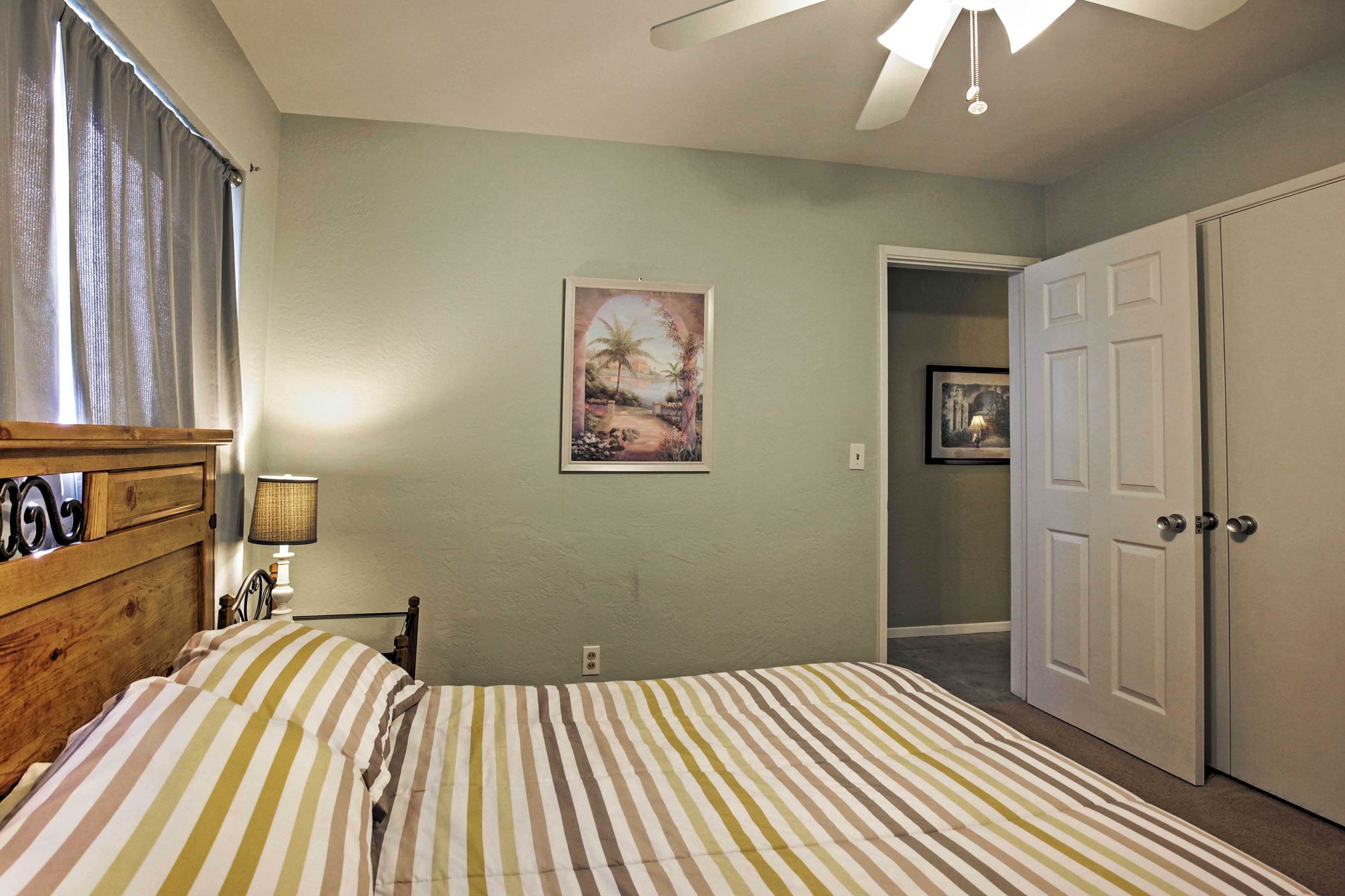A bedroom with a bed, a nightstand, a lamp, a framed picture on the wall, and a door to another room.