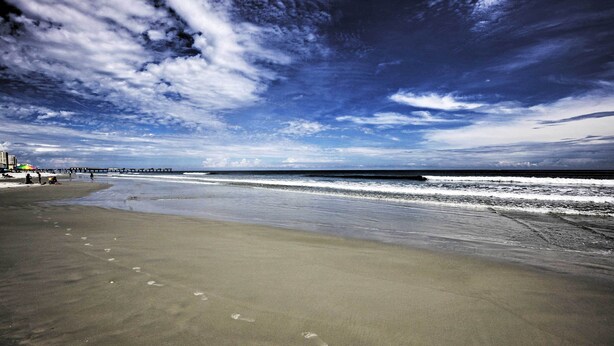 A beach with a pier extending into the ocean, sandy shore, and footprints in the sand. - Pet-friendly Daytona Beach Home, Walk to the Ocean (Port Orange)