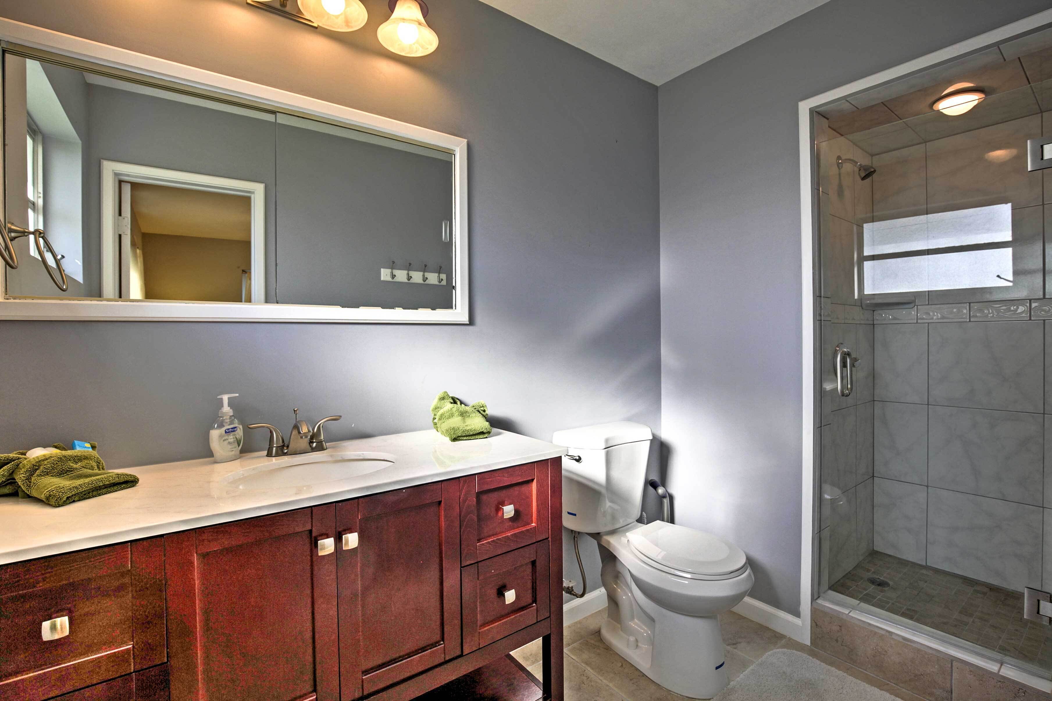 A bathroom with a vanity, sink, mirror, toilet, and a shower area.