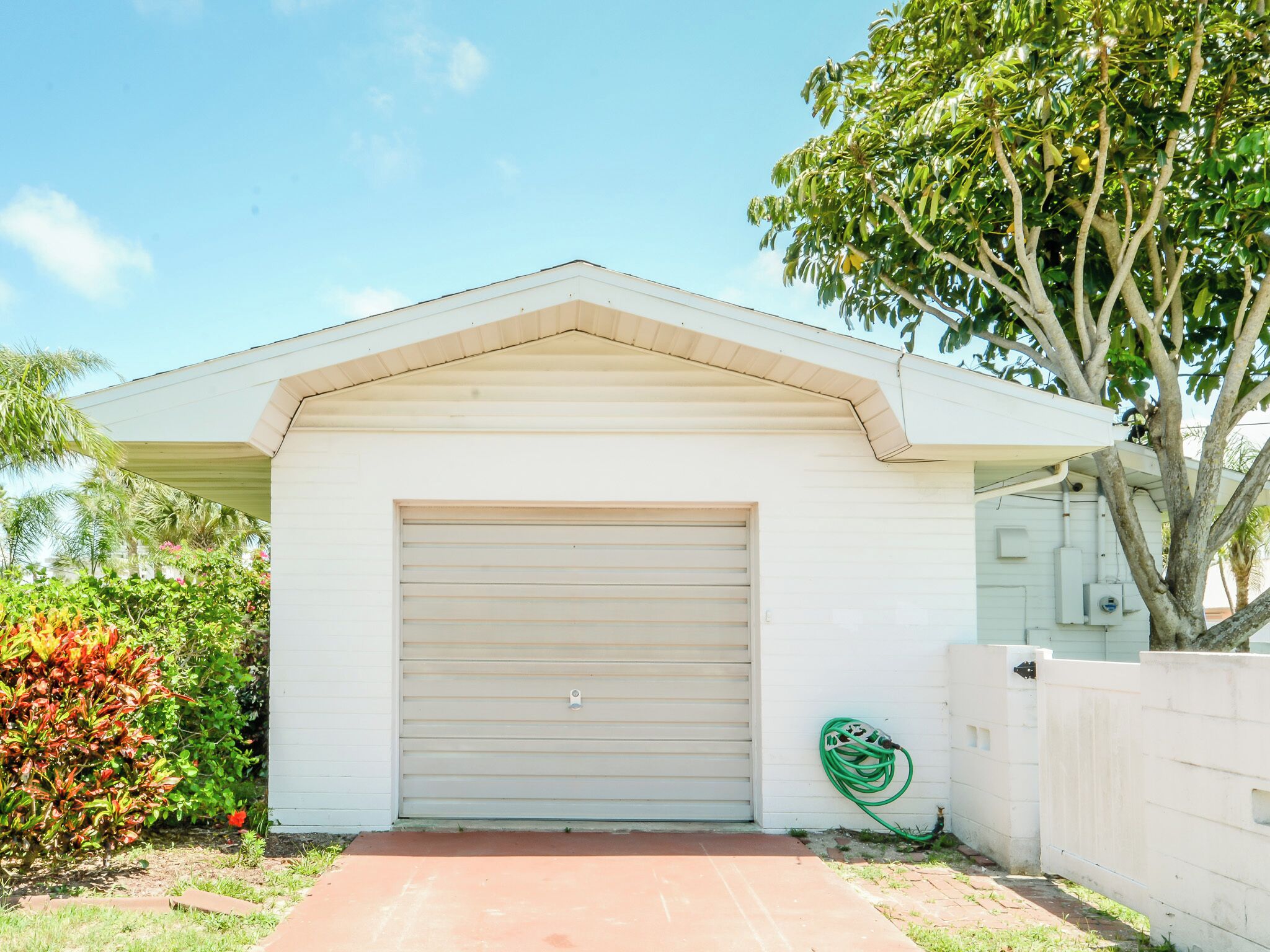 A single-story building with a closed garage door, a small porch area, and a tree in the background.