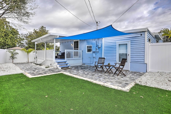 A blue house with a covered patio, a white fence, and a lawn.