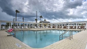 A pool area with lounge chairs and palm trees, surrounded by a covered pavilion. - Lanai & Resort Amenities: The Villages Getaway (Wildwood)