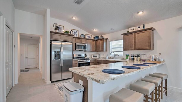 A modern kitchen with a central island, stainless steel appliances, and wooden cabinetry. - Lanai & Resort Amenities: The Villages Getaway (Wildwood)